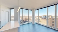Located in the Lincoln Park neighborhood of Chicago, this modern unit at 930 W Altgeld St offers a sleek, contemporary design across a single floor. The open living area is anchored by dramatic floor-to-ceiling corner windows that frame expansive rooftop views of the surrounding cityscape, flooding the space with natural light and creating an airy atmosphere. Smooth blue-toned hardwood flooring runs throughout the main living and hallway areas, complementing the crisp white walls and clean architectural lines.

The kitchen is thoughtfully designed with a combination of high-gloss white upper cabinetry and warm wood-tone lower cabinets, a tiled backsplash, stainless steel appliances including a gas range and refrigerator, and a generous island with a white quartz countertop. A pendant light fixture adds a refined touch above the workspace.

The hallway leads to the bedroom, which features large built-in closets and access to an in-unit laundry area. The bathroom is finished with a double-sink vanity topped with white countertops, warm wood-grain cabinetry, a large mirror, and clean tile flooring, giving it a spa-like feel. Throughout the unit, the minimalist design palette and abundant natural light create a cohesive, modern living environment.