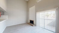 Located at 5604 Cotswold Hills Dr in Fort Worth, TX, this two-floor home offers a thoughtfully laid-out interior across two levels of living space. The main floor is anchored by a spacious, light-filled living room distinguished by dramatically high ceilings that amplify the sense of openness. A classic brick fireplace with a raised hearth serves as a focal point, framed by a tall white paneled surround. Light luxury vinyl plank flooring runs throughout, complementing the neutral, warm-toned walls. Sliding glass doors fitted with vertical blinds lead to a private balcony, inviting natural light and outdoor views into the living area. A pass-through window connects the living room to the kitchen, which features gray cabinetry, marble-style countertops, a stainless steel sink, tile flooring, and black appliances including a refrigerator and electric range. A stacked washer/dryer unit is also accommodated within the kitchen area. A ceiling fan with a textured popcorn ceiling adds character to the living zone. The upper floor includes a hallway, a walk-in closet with built-in shelving, and a bathroom with tile finishes. The 3D model reveals a compact, efficiently designed two-story layout with a staircase connecting both levels seamlessly.