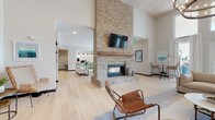 This thoughtfully designed single-floor amenity space offers an expansive, open-concept layout that seamlessly connects multiple functional zones. At the heart of the space stands a dramatic floor-to-ceiling brick fireplace with a reclaimed wood mantel and a mounted flat-screen TV, anchoring the main lounge area with warmth and visual impact. Soaring ceilings with wood-paneled accents amplify the sense of volume, while light wide-plank hardwood flooring flows consistently throughout, unifying each area.

The lounge features generous seating arrangements, including leather chairs and neutral sofas, creating inviting gathering spots. Large glass garage-style doors in the adjoining area flood the space with natural light and open to exterior views, effortlessly blending indoor and outdoor living. High-top seating near these doors adds a casual, social atmosphere.

The fully equipped kitchen is a standout feature, finished with sage green cabinetry, a textured white tile backsplash, and a waterfall-edge quartz island with bar seating. Stainless steel appliances, double wall ovens, and pendant lighting complete the functional yet stylish space.

A dining area accommodates group gatherings around a rustic farmhouse table. A display shelving unit and thoughtfully curated décor throughout contribute to the space's cohesive, contemporary coastal aesthetic.