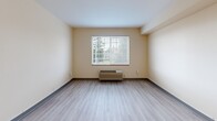 Located at 2752 NE Hogan Dr in Gresham, Oregon, this efficiently designed studio unit makes smart use of its compact footprint across a single floor. The open-plan layout seamlessly connects the kitchen and living area, creating a cohesive and functional living space.

The kitchen is well-appointed with white shaker-style cabinetry, light gray countertops, and a full suite of stainless steel appliances including an electric range, over-the-range microwave, dishwasher, and full-size refrigerator. Track lighting overhead provides ample illumination for cooking and dining. Light wood-style luxury vinyl plank flooring runs throughout the kitchen and living area, lending a clean, modern aesthetic.

The living area is open and bright, anchored by a large window fitted with horizontal blinds that frame views of the surrounding greenery. A wall-mounted HVAC unit ensures year-round climate comfort. Warm beige tones on the walls contribute to an inviting atmosphere.

The bathroom is finished with light ceramic tile flooring and features a full tub-shower combo with chrome fixtures, a toilet, and a vanity with a single-basin sink, gray countertop, white cabinetry, and a large framed mirror. A ventilation grate and towel rack complete the functional space.

Overall, the unit presents a tidy, move-in-ready environment with a clean, contemporary feel suited for efficient single-occupant living.