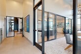Located at 3461 La Cadena Dr in Riverside, CA, this single-floor amenity space is a thoughtfully designed community hub that blends modern aesthetics with functional versatility. The layout encompasses a hallway and several distinct areas connected by dramatic floor-to-ceiling black-framed glass walls and doors that promote transparency and openness throughout.

The main lounge area features herringbone wood-patterned flooring, sculptural starburst pendant lighting, and a striking botanical wall mural. A large sectional sofa and curated accessories create an inviting social atmosphere. Adjacent to the lounge, a stylish bar and kitchen area offers a concrete-topped island with bar seating, custom cabinetry, and a dramatic living green wall installation overhead.

A dedicated conference room provides a polished setting for meetings, complete with a long dark wood table, rounded upholstered chairs, a wall-mounted display, and wood-paneled built-ins with teal accents. The game room is highlighted by soaring ceilings, oversized windows offering expansive outdoor views, a pool table, and a tiered chandelier.

Near the entrance, a bright reception-style lounge with a light wood credenza and patterned carpet tiles offers direct outdoor patio visibility. Throughout, the space maintains a cohesive modern design with warm neutral tones, abundant natural light, and high-end finishes.