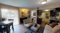 This single-story, one-bedroom, one-bathroom unit offers a thoughtfully organized layout that maximizes its compact footprint. The living area features warm wood-style flooring, a textured ceiling, and a sliding glass door fitted with vertical blinds that allows natural light to fill the space. An accent wall adds a pop of color, complementing the neutral tones throughout. A dedicated dining area near the entryway provides space for a small table and chairs, while a wet bar or secondary counter area with dark cabinetry and a sink adds functional versatility to the living space.

The galley-style kitchen is efficiently designed with dark espresso cabinetry lining both sides, laminate countertops, wood-style flooring, and white appliances including a refrigerator, range, and dishwasher, offering ample storage and prep space.

The bedroom is carpeted and includes a ceiling fan with light fixture, a mirrored closet, and a window that brings in natural light. The full bathroom features a tiled shower-tub combination. Throughout the unit, the consistent use of warm tones and wood-style flooring creates a cohesive and inviting ambiance.