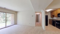 Located at 5 Maidstone Ct in Rosedale, Maryland, this single-floor residence offers a well-organized layout designed for comfortable everyday living. The main living area is generously proportioned, featuring soft neutral carpet, vaulted ceilings that enhance the sense of openness, and a sliding glass door that floods the space with natural light and provides direct access to a lush, wooded outdoor setting. A hallway leads from the living area deeper into the unit, where built-in shelving provides convenient storage.

The kitchen is efficiently designed with warm wood cabinetry, granite-look countertops, tile flooring, and a full suite of black appliances including a refrigerator, range, and built-in microwave. The space is practical and well-appointed for everyday cooking needs.

The bedrooms are carpeted and bright, with one featuring a window overlooking mature trees and the benefit of dual closets offering ample storage. Additional rooms provide versatile spaces that can serve as a bedroom, office, or flex room, each finished with neutral carpet and clean white walls.

The bathroom includes a wood-tone vanity with a granite-look countertop, an undermount sink, and mirrored medicine cabinets, providing a clean and functional finish. Throughout the residence, neutral tones and natural light create a calm, welcoming atmosphere.