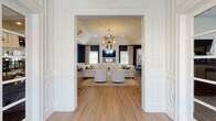 Located at 45 Farm Rd in Hillsborough, NJ, this single-floor community space combines classic architectural detailing with a refined, contemporary aesthetic. The interior is defined by a striking navy blue and crisp white color palette, carried consistently throughout each area and complemented by warm hardwood-style flooring.

The main lounge area is a standout feature, boasting soaring vaulted ceilings adorned with an eye-catching sculptural chandelier. Generous natural light filters through multiple windows dressed with flowing linen drapes, illuminating the elegantly arranged seating — including plush cream sofas, swivel chairs, and patterned accent rugs. A wall-mounted flat-screen TV above a linear fireplace serves as a central focal point, while wainscoting and crown molding add a polished architectural character.

A welcoming entry lounge provides additional seating with coordinated furnishings, wall sconces, and curated artwork, creating a warm first impression for guests and residents alike.

The kitchen is well-appointed with white shaker cabinetry, quartz countertops, a subway tile backsplash, and black hardware accents. A central island with bar seating offers a functional and social gathering spot, while stainless steel appliances and a window above the sink ensure both practicality and natural light. A glass-paneled exterior door provides convenient outdoor access.