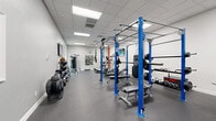 Located at 518 Lake Bridge Ln in Apopka, Florida, this dedicated fitness center offers a comprehensively outfitted exercise space designed to support a wide variety of workout routines. The single-floor layout is finished with durable rubber flooring throughout, providing a safe and functional surface for all types of training activities.

The space is organized to maximize usability, with distinct zones for strength training and cardiovascular exercise. A prominent blue power rack with an attached pull-up bar and TRX suspension system serves as the centerpiece, accompanied by a weight bench, barbell set, and an assortment of kettlebells. A tiered dumbbell rack offers a wide range of free weights, while a medicine ball tower adds versatility for functional training. A cable machine provides additional strength options.

The cardio section features multiple treadmills, an elliptical trainer, a stair climber, and a stationary bike, ensuring ample options for aerobic workouts. A wall-mounted flat-screen television enhances the exercise experience. A cable-style multi-function machine rounds out the strength equipment offerings.

The room is brightly lit by recessed panel ceiling lights and benefits from natural light through a window with outdoor views of surrounding greenery. Clean white and gray walls, a drop ceiling, and a well-organized layout contribute to an efficient and welcoming atmosphere suited for community or residential fitness use.