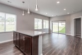 This well-appointed single-floor unit offers a thoughtfully designed open-concept layout that seamlessly connects the living and kitchen areas. Rich, dark hardwood-style flooring flows throughout the main living spaces, providing a warm and polished aesthetic that ties the interior together.

The kitchen is a standout feature, outfitted with dark espresso cabinetry, granite countertops, and a full suite of stainless steel appliances including a refrigerator, dishwasher, microwave, and range. A distinctive penny-tile backsplash adds a modern touch, while pendant lighting above the island and recessed ceiling lights ensure the space is well-lit. Multiple windows with blinds invite natural light and offer outdoor views of greenery.

The living area is spacious and bright, with sliding glass doors leading to an outdoor green space, further enhancing the sense of openness. Neutral gray walls complement the flooring and create a versatile backdrop for any interior style.

The bathroom is clean and functional, featuring matching espresso cabinetry, granite countertops, and durable flooring consistent with the rest of the unit. An adjacent walk-in closet provides ample storage. The dollhouse view confirms a compact yet efficient floor plan with a well-defined bedroom, bathroom, and open living-kitchen zone.