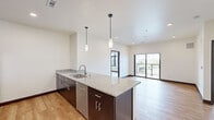 This modern single-floor unit showcases a thoughtfully designed open-concept layout with clean lines and contemporary finishes throughout. The kitchen serves as the centerpiece, featuring a large granite-topped island with a stainless steel sink, dark espresso cabinetry, a subway tile backsplash, and a full suite of stainless steel appliances including a refrigerator, range, microwave, and dishwasher. Stylish pendant lighting hangs above the island, adding a warm, modern touch. Light hardwood flooring flows seamlessly through the kitchen and living areas, creating a bright, cohesive feel.

The living area opens to a private balcony through sliding glass doors, offering expansive outdoor views that bring natural light deep into the space. A second balcony access point is also present, further enhancing the connection to the outdoors.

The bedrooms are finished with plush carpeting and feature generous walk-in closets with built-in wire shelving. Large windows in the bedroom areas frame scenic views of the surrounding cityscape. Two bathrooms serve the unit, each outfitted with granite-topped vanities, dark cabinetry with brushed nickel hardware, and hardwood-style flooring, maintaining the cohesive modern aesthetic found throughout the entire space.