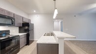Located at 5500 Hildebrand Rd. in Columbus, OH, this one-bedroom, one-bathroom unit offers a well-designed single-floor layout with a thoughtful mix of modern finishes and functional living spaces. The kitchen is a standout feature, showcasing dark cabinetry, marble-look countertops, a double-basin sink, a peninsula with pendant lighting, and stainless and black appliances including a range, microwave, dishwasher, and refrigerator. Light wood-style flooring runs throughout the kitchen and main areas, lending a clean, contemporary feel. The open layout connects the kitchen seamlessly to the living room, which is carpeted, ceiling fan-equipped, and features a set of glass French doors that open to an outdoor balcony, inviting in natural light and outdoor views. The bedroom is carpeted and comfortably sized, benefiting from a natural light source through its window and a sliding-door closet with wire shelving. Two closets in total provide ample storage. The bathroom includes a full tub/shower combo with chrome fixtures and a marble-look vanity countertop. A dedicated laundry room with wire shelving and appliance hookups adds everyday convenience. The hallway connects the rooms efficiently, completing this well-appointed Columbus residence.