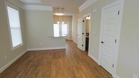 This two-story space offers a thoughtfully designed interior that balances comfort and functionality. The main level features warm hardwood-style flooring that flows seamlessly throughout the open-concept living and dining areas, creating a cohesive and inviting atmosphere. Crown molding adds a refined architectural detail along the ceilings, complementing the neutral, earthy wall tones that lend a calm and welcoming ambiance.

A kitchen peninsula with a granite-style countertop serves as both a practical workspace and a casual dining spot, anchored by a trio of pendant lights hanging above. Natural light filters in through a window near the dining area, brightening the space and enhancing its open feel. White-paneled doors with dark hardware provide a clean contrast to the warm flooring and soft wall colors throughout.

A glimpse into an adjacent room reveals a sink and vanity area, suggesting a well-placed bathroom conveniently accessible from the main living space. The overall layout is open and airy, with clear sightlines between rooms that enhance the sense of spaciousness. Spanning two floors, this space provides ample room across multiple levels, making it well-suited for a variety of living arrangements and functional needs.