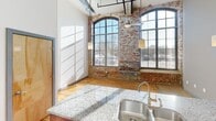 This 560 square foot loft-style apartment in Charlotte, NC, combines industrial charm with modern amenities. The space features soaring ceilings with exposed ductwork and large arched windows that flood the interior with natural light. The open-concept living area showcases original brick walls, hardwood floors, and a sleek kitchen with granite countertops and stainless steel appliances. The single bedroom measures 130 square feet, while the bathroom boasts a contemporary design with a granite vanity. Located at 1111 Hawthorne Ln, this unique urban dwelling offers an efficient layout that maximizes space and style in its compact footprint.