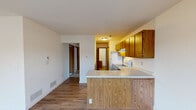 This single-floor residence offers a functional and comfortable layout with a clean, neutral aesthetic throughout. The open living area greets you upon entry, featuring light wood-look vinyl flooring and a large window that draws in natural light and provides views of the surrounding neighborhood. The kitchen is appointed with warm-toned wood cabinetry, light countertops, a peninsula that doubles as additional prep space, and white appliances including a refrigerator and electric range. A hallway from the kitchen connects to the rest of the home, maintaining a practical flow between spaces. The bedrooms are carpeted in soft gray, offering a cozy feel, and include built-in sliding wood closets for ample storage. Windows in the bedrooms allow natural light to filter in, further brightening each room. The bathrooms are finished in clean white tones — one features a full tub and shower combo with chrome fixtures, while another serves as a half bath with a pedestal-style sink, toilet, and wood-look flooring. Throughout the residence, white walls and bright trim create a consistent, move-in-ready appearance. The overall ambiance is straightforward and practical, offering a solid foundation for comfortable everyday living.