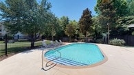 Situated at 200 Colony Park Drive in Pearl, Mississippi, this single-story property offers a welcoming and well-appointed environment. The standout feature of the space is its outdoor swimming pool, which is generously sized with a classic geometric shape and finished with a striking blue tile accent along the entry steps. Stainless steel handrails provide safe and convenient access into the pool.

The surrounding pool deck is paved with a light-toned surface, offering ample space for relaxation. Several lounge chairs are positioned poolside, creating a comfortable setting for outdoor leisure. The pool area is enclosed by a black iron fence, providing both security and a clean, defined perimeter.

Lush, mature trees—including what appear to be magnolias and hardwoods—frame the entire area, offering natural shade and a sense of privacy. The well-maintained green lawn visible beyond the fence adds to the overall appeal of the outdoor environment. The space benefits from abundant natural light under open skies, enhancing the bright and refreshing atmosphere.

Overall, the property presents a clean, functional, and inviting outdoor amenity space well-suited for warm-weather enjoyment in the Pearl, Mississippi area.