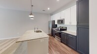 Located at 15902 White St in Charlotte, NC, this single-floor home offers a well-designed, open-concept layout with modern finishes throughout. The kitchen serves as a central highlight, featuring a large granite-topped island with an undermount sink and stylish pendant lighting overhead. Crisp white upper cabinetry contrasts with dark lower cabinets, while stainless steel appliances — including a French door refrigerator with ice maker, electric range, and built-in microwave — provide a sleek, functional workspace. A subway tile backsplash adds a clean, contemporary detail. Wood-look flooring runs through the kitchen and connects seamlessly to the adjoining areas. The living space is generously sized and finished with plush wall-to-wall carpeting, neutral walls, and recessed lighting, creating a bright and welcoming atmosphere. Natural light enters through windows with outdoor views, enhancing the open feel of the room. The bathroom is well-appointed with a tiled soaking tub and shower combination, a dark-framed vanity mirror, granite countertop vanity with ample drawer storage, and wood-look flooring that ties the space together. Throughout the home, dark-paneled interior doors provide a sharp contrast against the light, neutral palette, lending the space a polished and cohesive aesthetic.