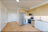 Located at 431 Dr. Martin Luther King Jr. Boulevard in East Orange, NJ, this efficiently designed studio unit offers a well-planned single-floor layout that maximizes every square foot. The open-concept kitchen and living area serves as the heart of the space, featuring light wood laminate flooring that extends throughout. The kitchen is outfitted with modern two-tone cabinetry — warm natural wood upper cabinets paired with clean white lower cabinets — and stainless steel appliances including a refrigerator, electric range, over-the-range microwave, and dishwasher. Light gray countertops and a stainless steel sink complete the functional and contemporary kitchen design. The living area benefits from a large window that invites natural light and provides elevated views of the surrounding East Orange neighborhood. A wall-mounted HVAC unit ensures year-round climate control. The full bathroom features a white vanity with a wide mirror, tile flooring, and clean white walls with chrome fixtures. Additional conveniences include a dedicated closet for storage and an in-unit laundry area. The overall aesthetic is modern and bright, with a neutral white and light wood palette that creates a clean, move-in-ready atmosphere.