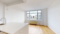 Located on the 15th floor of 21 Chelsea in New York City, this 440-square-foot one-bedroom, one-bathroom apartment offers a well-designed layout across a single floor. The combined kitchen and living area serves as the heart of the unit, featuring warm hardwood flooring throughout and large floor-to-ceiling windows that flood the space with natural light while framing impressive views of the surrounding Manhattan skyline. The modern kitchen is equipped with stainless steel appliances, including a full-size refrigerator, gas range, and built-in microwave, complemented by natural wood cabinetry and a white quartz peninsula countertop that provides additional workspace and casual dining options. The 130-square-foot bedroom continues the hardwood flooring and benefits from oversized windows showcasing expansive city views, along with a double-door closet for ample storage. The bathroom features a clean, contemporary design with large neutral wall tiles, a soaking tub with overhead shower, a wall-mounted wood vanity with an undermount sink, and a window offering natural light and ventilation. Throughout the unit, crisp white walls and a neutral palette create a bright, airy ambiance well-suited for urban living.