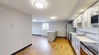 Located at 101 Cedar St in Providence, Rhode Island, this single-floor unit offers a thoughtfully designed layout with a blend of modern finishes and functional living spaces. The open-concept kitchen and living area is anchored by warm wood-look flooring, neutral gray walls, and flush-mount ceiling lighting. The kitchen is well-equipped with white shaker-style cabinetry, light countertops, a subway tile backsplash with a decorative mosaic accent, and a full suite of stainless steel appliances including a refrigerator, dishwasher, range, and microwave. A central kitchen island provides additional workspace and storage. The open living area benefits from natural light through a window and baseboard heating along the perimeter. Bedrooms feature plush patterned carpeting, built-in storage cabinetry, and windows offering elevated views of the Providence cityscape and surrounding neighborhood. One bedroom includes a wall air conditioning unit for added comfort. The bathrooms are clean and functional, featuring walk-in shower stalls with white surround walls, subway tile accents, and chrome fixtures — one bathroom includes a grab bar for accessibility. Throughout the unit, dark baseboards provide a sharp contrast against the light walls and flooring, contributing to a crisp, modern aesthetic.