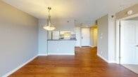 Located on the third floor at 9890 Washingtonian Blvd in Gaithersburg, MD, this apartment offers a thoughtfully designed single-level layout with a comfortable and functional flow throughout. The open living and dining area is anchored by warm hardwood flooring and features a elegant pendant light fixture, creating an inviting atmosphere. Sliding glass doors lead to a private balcony, allowing natural light to fill the space and offering views of the surrounding greenery. The galley-style kitchen is positioned behind a half-wall peninsula with dark countertops, and is equipped with white cabinetry featuring gold hardware, a matching white refrigerator, range, and a built-in sink — providing ample storage and workspace. The bedroom is carpeted for comfort and benefits from a large window with outdoor views, contributing to a bright and airy feel. The bathroom is appointed with a striking dark marble vanity countertop, a framed mirror, and well-placed lighting above the sink, complemented by a shower with a curtain enclosure. Neutral gray walls throughout the unit, textured ceilings, and clean white trim tie the overall aesthetic together, creating a cohesive and move-in ready living space.