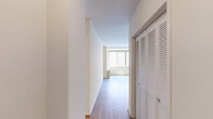 Located at 925 25th St NW in Washington, DC's Foggy Bottom neighborhood, Unit 215 is a one-bedroom, one-bathroom residence with a well-organized, single-floor layout. The living room is bright and welcoming, featuring light hardwood flooring and a wide bank of windows that invite natural light and provide views of the surrounding brick exterior. A wall-mounted HVAC unit ensures year-round comfort. The open sightline from the living area leads to a compact kitchen, which is outfitted with white cabinetry, a gas range, and a peninsula-style counter — efficient and practical in its design. The spacious bedroom is carpeted for warmth and comfort, featuring its own set of large windows that continue the natural light theme throughout the unit. A wall-mounted heating unit is also present in the bedroom. The bathroom is clean and simply appointed, with classic white tile surrounding a full bathtub and shower combination, mosaic tile flooring, and a pedestal-style sink. A hallway connects the rooms with ease, offering a logical flow through the residence. The neutral color palette and clean lines throughout create a calm, functional ambiance well-suited for everyday living in the heart of Washington, DC.