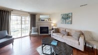 This single-floor residence offers a thoughtfully designed layout with a warm, cohesive aesthetic carried throughout each room. The living room serves as the heart of the home, anchored by a classic fireplace with a mirrored mantle, rich hardwood flooring, and a sliding glass door that opens to an outdoor patio, filling the space with natural light and views of the surrounding area. The kitchen is well-equipped with warm oak cabinetry, stainless steel appliances including a refrigerator, range, and microwave, granite-style countertops, and a peninsula with bar seating — ideal for casual dining or entertaining. A dedicated flexible room features hardwood flooring, a built-in closet, and ample space to serve as a home office or additional sleeping area. The primary bedroom offers plush carpeting, a ceiling fan, natural light from a window with outdoor views, and direct access to a private en-suite bathroom. A second bedroom is equally comfortable with carpet, a ceiling fan, and bright windows. The bathroom features a granite-topped vanity with warm wood cabinetry, a tub-shower combination, and hardwood flooring. Throughout the residence, neutral tones and consistent finishes create a calm, inviting ambiance.