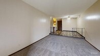 Located at 4008 S Louise Ave, Unit 305 in Sioux Falls, SD, this one-bedroom, one-bathroom unit offers a practical and comfortable layout across a single floor. The interior is defined by a distinctive split-level design, with wood-style plank flooring in the entry and kitchen area transitioning to plush carpeting in the living and sleeping spaces. A textured ceiling and iron railing detail add character to the living area, which is brightened by a large sliding window and a ceiling fan with an integrated light fixture. The spacious living room receives generous natural light and provides a welcoming, open atmosphere. The kitchen features wood-toned cabinetry and an open connection to the main living area, ensuring a functional flow throughout the unit. The well-sized bedroom is carpeted, naturally lit by a window, and served by a dedicated closet for storage. The full bathroom includes a single-sink vanity with wood cabinetry, a toilet, and a shower/tub combination with a clean white surround. Neutral wall tones and baseboard heating are consistent throughout, contributing to a cohesive and comfortable living environment. A hallway connects the main areas, completing this efficiently designed residential unit.