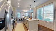 Located at 2200 Silver Crescent Dr in Charlotte, NC, this single-floor residence offers a thoughtfully designed open-concept layout with modern finishes and abundant natural light throughout. The kitchen serves as the heart of the home, centered around a large white island with seating, white shaker-style cabinetry with black hardware, stainless steel appliances, a herringbone tile backsplash, and stylish pendant lighting. The kitchen flows seamlessly into the dining area, which features a chandelier and large windows, and connects to the living room, where two bright windows, warm hardwood-style flooring, and a cozy, contemporary aesthetic create an inviting atmosphere. The bedrooms are carpeted and well-lit by generous windows with blinds and curtains, offering comfortable, private retreats. One bedroom features a distinctive blue accent wall and wall-mounted sconce lighting. The bathrooms are finished with light cabinetry, white countertops, black fixtures, wood-look flooring, and large mirrors, providing a clean, modern feel. Additional features include a dedicated closet space and consistent hardwood-style flooring in the common areas. The home's neutral palette, modern lighting fixtures, and abundant windows combine to create a bright, welcoming living environment throughout.