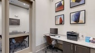 Located at 2906 Delafield St in Houston, TX, this single-floor office space offers a thoughtfully designed environment suited for both focused individual work and collaborative meetings. The space is divided into two functional areas: a private conference room and a personal workstation nook.

The conference room is the centerpiece of the space, featuring a substantial dark wood table surrounded by upholstered chairs in neutral tones. A wall-mounted flat-screen display supports presentations and virtual meetings, while a wall-mounted camera enhances connectivity. Tall glass-paneled doors with transom windows flood the room with natural light and provide a visual connection to the adjoining common area, contributing to an open and airy atmosphere. Bold, colorful artwork adorns one wall, adding a creative energy to the professional setting.

Adjacent to the conference room is a compact workstation area, equipped with a built-in granite-topped desk, dark cabinetry below for storage, a desktop computer, and a printer. The wall above the desk is decorated with a curated set of geometric abstract art prints, lending a refined aesthetic to the workspace.

Throughout, soft neutral walls, light gray carpet, and clean architectural finishes create a cohesive, modern, and professional ambiance ideal for productivity.