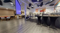 Located on Dunn Drive in Los Angeles, this single-floor commercial space delivers a thoughtfully designed environment suited for events, meetings, and collaborative gatherings. The open main hall features soaring ceilings with exposed ductwork and an eclectic mix of suspended acoustic panels, pendant lights, and a mirrored disco ball, creating a dynamic industrial-modern aesthetic. A large projection screen anchors one wall, bathed in ambient purple lighting that adds a dramatic focal point to the space.

A raised multi-level platform at the center of the room, framed by geometric metal railings, provides flexible staging or presentation options. Cocktail-height tables nearby support a versatile event layout. To one side, a built-in kitchenette bar with wood cabinetry, counter seating, and beverage service equipment offers convenient hospitality functionality.

A separate lounge area transitions into a more intimate setting, featuring tall frosted glass panels with integrated LED strip lighting, textured accent walls, and a curated mix of seating including a low sectional sofa, bold red accent chairs, and modular wood coffee tables. Additional casual dining clusters with round tables and mixed-color chairs provide further flexibility throughout the space. The overall ambiance balances energetic event-ready design with comfortable, inviting lounge functionality.