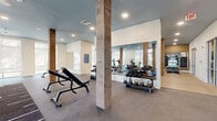 Located at 1804 Appaloosa Ln in Buford, Georgia, this expansive fitness center offers a well-appointed, single-floor layout designed to support a wide range of workout activities. The space is divided into distinct functional zones, each thoughtfully outfitted for different training needs.

The main strength and cardio area features durable concrete flooring, rustic wood-wrapped columns, and floor-to-ceiling mirrors that amplify the sense of space. A comprehensive selection of free weights — including dumbbells and kettlebells on tiered racks — is complemented by adjustable benches, a cable machine, and a punching bag. Treadmills, ellipticals, and stationary bikes line the perimeter near large windows dressed with roller shades, allowing ample natural light to fill the room.

A separate group exercise and studio area showcases warm hardwood flooring, wood-paneled accent walls, and additional mirrors. This open zone accommodates yoga, stretching, and functional training, with ceiling fans overhead and medicine ball storage along the walls.

Throughout the facility, a signature blue-painted ceiling creates a cohesive, contemporary aesthetic that contrasts beautifully with white shiplap walls and the natural wood column accents. Recessed lighting and ceiling fans ensure comfort across all areas. The overall ambiance is modern yet inviting, making this fitness center a well-equipped destination for residents seeking a complete and elevated wellness experience.