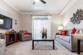 This single-floor residence offers a thoughtfully designed layout that balances comfort and functionality across several well-defined living spaces. The living room serves as the heart of the home, finished with plush carpeting, crown molding, and a ceiling fan. A sliding glass door opens to a private balcony, filling the room with natural light and providing outdoor views. The galley-style kitchen features light wood cabinetry, white appliances including a range, refrigerator, and dishwasher, complemented by wood-look flooring and generous counter and storage space on both sides. Adjacent to the kitchen, a dedicated dining area provides space for full-size dining furniture. The primary bedroom is generously sized with multiple windows, soft carpet, a ceiling fan, and a vanity area complete with a wide mirror, built-in sink, and ample cabinet storage. A secondary bedroom mirrors this comfort with its own window, ceiling fan, and carpeted flooring. The bathrooms are well-appointed, with one featuring a combination tub and shower with sliding glass doors and wood-look flooring. Throughout the residence, neutral tones and consistent finishes create a cohesive and inviting ambiance.