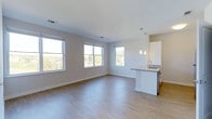 This single-floor, 2-bedroom, 2-bathroom residence offers a clean, contemporary design throughout. The open-concept living and kitchen area is anchored by light hardwood flooring that runs seamlessly across the space, creating a cohesive and airy feel. Multiple large windows flood the interior with abundant natural light while framing pleasant views of surrounding greenery, enhancing the sense of openness.

The kitchen is integrated into the main living area and features a peninsula with a granite or stone-topped counter, an undermount sink, and pendant lighting overhead — providing both functional workspace and a natural division between the kitchen and living zones. White cabinetry and modern finishes contribute to the unit's bright, fresh aesthetic.

The neutral, light gray walls complement the flooring and trim throughout, maintaining a consistent and inviting palette. Recessed lighting supplements the natural light, ensuring the space is well-lit at any time of day. The overall layout is thoughtfully designed to maximize usable space while maintaining an open, uncluttered atmosphere, making it a versatile and comfortable living environment.