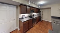 This single-floor residence offers a thoughtfully designed layout that balances open living areas with functional private spaces. The living room features warm hardwood flooring, neutral beige walls, and ample room for comfortable seating arrangements, creating an inviting atmosphere for relaxation or entertaining.

The kitchen is a standout feature, showcasing rich dark-wood cabinetry, dark granite countertops, and a full suite of stainless steel appliances including a range, built-in microwave, refrigerator, and dishwasher. Track lighting illuminates the space, while hardwood flooring continues throughout, lending a cohesive aesthetic.

The bedroom is generously sized, finished with plush carpeting, neutral tones, and a window that allows natural light to filter in, contributing to a calm and restful environment.

The full bathroom is well-equipped with a soaking tub framed in tile surround, a separate vanity area, and tile flooring throughout. An additional utility area provides in-unit laundry connections with wire shelving for storage. Together, these spaces form a well-rounded, comfortable residence.