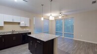 Located at 1777 Harvard Ave in College Park, GA, this single-floor residence offers a well-designed open-concept layout that seamlessly connects the kitchen and living areas. The kitchen is a standout feature, showcasing dark espresso cabinetry paired with crisp white upper cabinets, granite countertops, a center island with pendant lighting overhead, and black appliances including a refrigerator, range, microwave, and dishwasher. Wood-style flooring runs throughout the main living areas, adding warmth and continuity to the space. Large windows and sliding glass doors flood the living area with natural light and provide views of the outdoors, while a ceiling fan adds comfort overhead. The bedrooms offer plush carpeting, ceiling fans, and ample closet space, with windows that bring in natural light. The bathrooms are finished with large-format tile flooring, dark vanity cabinetry with white countertops, and well-lit mirrors. One bathroom features a full soaking tub with a white tiled surround. The neutral color palette and consistent use of quality finishes throughout create a cohesive and modern ambiance across the entire residence.