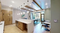 Located at 1508 Clare Lane in Wayzata, Minnesota, this thoughtfully designed single-floor amenity space offers a compelling blend of entertainment and social functionality. The open layout accommodates multiple activity zones, creating a versatile gathering environment with a cohesive, upscale aesthetic throughout.

At the heart of the space is a striking kitchen and bar area, anchored by a long island with a bold teal base and white countertop, lined with walnut barstools upholstered in dark leather. Behind the bar, warm oak cabinetry with arched glass display shelves flanks a wall-mounted television set against a vertical teal tile backsplash. Pendant lighting with sculptural glass shades adds a refined, boutique ambiance overhead.

The game area features a solid wood pool table positioned atop a textured area rug, complemented by a shuffleboard table along the wall and curated artwork. Exposed wood ceiling beams and recessed lighting give the space architectural character, while shiplap ceiling detailing adds a subtle coastal touch.

A lounge nook with sage green paneled walls, built-in banquette seating, and framed landscape artwork provides an inviting retreat. Large black-framed glass doors open to an outdoor area, flooding the interior with natural light. Light wood-look flooring ties the entire space together, creating a warm, welcoming atmosphere throughout.