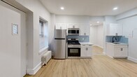 Located at 601 W Cliveden St in Philadelphia's Mt. Airy neighborhood, this single-floor 2-bedroom, 1-bathroom unit offers a clean, modern aesthetic throughout. Light wood luxury vinyl flooring runs consistently across every room, complemented by crisp white walls, white baseboards, and recessed lighting in key areas.

The entrance opens into a well-proportioned living area featuring a window with blinds and a classic cast-iron radiator. Two connecting hallways guide movement through the unit, providing efficient access to all rooms. The kitchen is a standout, outfitted with white shaker-style cabinetry, a light blue subway tile backsplash, white quartz countertops, and a full suite of stainless steel appliances including a gas range, over-the-range microwave, and refrigerator.

The spacious primary bedroom includes recessed lighting, a window for natural light, and dedicated closet access. The second bedroom features a window and a cast-iron radiator. The bathroom is finished with a geometric patterned tile accent wall, a soaking tub, dark slate floor tile, and a window for ventilation. A dedicated laundry area and additional closet storage add practical convenience to this well-appointed unit.