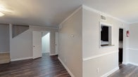This two-floor residence offers a well-organized layout with a blend of practical finishes and comfortable living spaces throughout. The main level features rich, dark hardwood-style flooring that flows through the open living area, hallways, kitchen, and bathrooms. The spacious living room is bright and airy, benefiting from multiple windows that invite natural light, and is anchored by a ceiling light fixture. A pass-through opening connects the living area to the galley-style kitchen, which is outfitted with dark espresso cabinetry, dark granite-style countertops, a double stainless steel sink, and black appliances including a refrigerator, stove, and microwave. The main-level bathroom features a dark vanity with granite-style countertops, a wide mirror with overhead lighting, and a tub-shower combination with clean white tile surround and hardwood-style flooring. Upstairs, the bedrooms are carpeted for warmth and comfort. The primary bedroom is particularly notable for its vaulted ceiling, ceiling fan, dual closets, and direct access to an outdoor balcony through sliding glass doors. Secondary bedrooms also include closet storage. A second bathroom with matching finishes serves the upper level. Crown molding and consistent neutral tones throughout contribute to a cohesive and polished aesthetic.