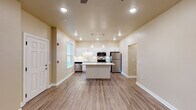 This single-floor residence offers a clean, modern aesthetic defined by warm neutral tones, white trim, and durable wood-look flooring throughout the main living areas. The heart of the home is an open-concept kitchen that showcases white shaker-style cabinetry, light stone countertops, and a full suite of stainless steel appliances, including a refrigerator, range, microwave, and dishwasher. A central island with pendant lighting above provides additional prep space and a natural gathering point. Recessed lighting and under-cabinet lighting ensure the kitchen is bright and functional at all hours.

The adjacent living area is generously proportioned, featuring a ceiling fan, recessed lighting, and a front entry door with a nearby window that brings in natural light and views of the surrounding greenery. The open layout creates a seamless flow between the kitchen and living spaces.

The bedrooms are finished with plush carpeting and ceiling fans, offering a comfortable retreat. Each bedroom benefits from natural light, with at least one featuring a large window framing pleasant outdoor views. The bathroom is neatly appointed with a grey vanity, white countertop, wood-look flooring, and brushed nickel hardware, reflecting a cohesive and contemporary design throughout the home.