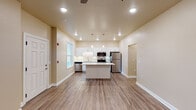 This single-floor residence offers a clean, modern aesthetic defined by warm neutral tones, white trim, and durable wood-look flooring throughout the main living areas. The heart of the home is an open-concept kitchen that showcases white shaker-style cabinetry, light stone countertops, and a full suite of stainless steel appliances, including a refrigerator, range, microwave, and dishwasher. A central island with pendant lighting above provides additional prep space and a natural gathering point. Recessed lighting and under-cabinet lighting ensure the kitchen is bright and functional at all hours.

The adjacent living area is generously proportioned, featuring a ceiling fan, recessed lighting, and a front entry door with a nearby window that brings in natural light and views of the surrounding greenery. The open layout creates a seamless flow between the kitchen and living spaces.

The bedrooms are finished with plush carpeting and ceiling fans, offering a comfortable retreat. Each bedroom benefits from natural light, with at least one featuring a large window framing pleasant outdoor views. The bathroom is neatly appointed with a grey vanity, white countertop, wood-look flooring, and brushed nickel hardware, reflecting a cohesive and contemporary design throughout the home.