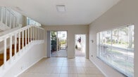 This two-story residence in Dania Beach, Florida offers a clean, neutral interior designed for comfortable everyday living. The main level features light ceramic tile flooring throughout the living and dining areas, which are bathed in natural light from multiple windows fitted with horizontal blinds. A sliding glass door opens directly to a private patio with decorative stonework and a gated entry, providing a seamless indoor-outdoor connection framed by lush tropical greenery.

The kitchen is a functional highlight of the home, outfitted with warm-toned wooden cabinetry, dark granite countertops, a breakfast bar peninsula, and a full suite of stainless steel appliances including a refrigerator, range, microwave, and dishwasher. Tile flooring continues throughout the kitchen, and a half bath is conveniently accessible nearby.

The staircase leads to the upper level, where the bedrooms feature light hardwood flooring and windows with views of the surrounding landscape. The bathrooms are finished with tile flooring, wooden vanity cabinetry, integrated sinks with light countertops, and one bathroom includes a tiled walk-in shower with sliding glass doors. Throughout, the home maintains a bright, understated aesthetic with white walls and clean finishes.