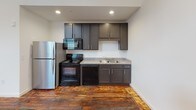 Located at 240 4th St in Inman, South Carolina, this single-floor space masterfully combines industrial character with contemporary finishes. Rich, reclaimed hardwood floors run throughout, adding warmth and texture to every room.

The open living area makes a striking impression with soaring ceilings clad in whitewashed wood planking, a whitewashed exposed brick accent wall, and a ceiling fan overhead. Flush and panel lighting illuminate the space, while the open layout offers generous room for a variety of uses.

The kitchen is efficiently appointed with dark gray cabinetry, granite-style countertops, and a full suite of black appliances including an electric range, dishwasher, and microwave, complemented by a stainless steel refrigerator. Recessed lighting keeps the workspace bright and functional.

A dedicated room provides a quiet, versatile space with large black-framed windows that invite natural light and views of the surrounding area. The whitewashed plank ceiling continues here, maintaining design consistency throughout.

The bathroom features a full tub and shower combination, a granite-topped vanity, and chrome fixtures, including a grab bar for added accessibility — all finished with clean white walls for a crisp, bright feel.

This space offers a compelling blend of historic character and modern utility in the heart of Inman, SC.