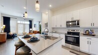 This well-designed single-floor residence offers a cohesive blend of modern aesthetics and functional living. The open-concept kitchen is a standout feature, showcasing crisp white shaker cabinetry, a white subway tile backsplash, grey quartz countertops, and a full suite of stainless steel appliances including a range, over-the-range microwave, and refrigerator. A central island with a deep undermount sink and pendant lighting above serves as both a prep space and casual dining area with bar seating. Light wood-tone flooring flows seamlessly throughout the main living areas, connecting the kitchen to a bright and inviting living room that features large windows with ample natural light, a ceiling fan, and curated wall art. The bedroom is generously proportioned, also benefiting from large windows and a ceiling fan, and connects directly to a spacious walk-in closet outfitted with multi-level shelving and hanging rods. The bathroom is finished to a high standard with a dual-sink vanity, a large mirror, and a soaking tub with a marble-tile surround. A dedicated in-unit laundry area with a full-size washer and dryer adds everyday convenience. Throughout, the space maintains a clean, contemporary palette with warm accent tones.
