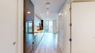 Located in San Diego's 92103 neighborhood, this thoughtfully designed unit offers a modern aesthetic across a single floor. The open-plan living and kitchen area is anchored by striking floor-to-ceiling windows and a glass sliding door that frames elevated city and skyline views, flooding the space with natural light. Light-toned hardwood flooring runs throughout, contributing to a clean, airy atmosphere.

The kitchen is a standout feature, showcasing a contemporary two-tone design with high-gloss dark lower cabinetry and matte taupe upper cabinets extending to the ceiling for maximum storage. Stainless steel appliances, including a gas range and built-in microwave, are complemented by white quartz countertops and a marble-effect tile backsplash. A stainless steel sink completes the functional layout.

The living area benefits from the same expansive glazing, with neutral white walls and recessed lighting reinforcing the modern, minimalist tone. A sliding closet door provides efficient storage within the compact footprint.

The bathroom is finished to a high standard, featuring large-format light stone-effect floor tiles, a frameless glass-enclosed walk-in shower with marble-style tile surround, and gold-toned hardware accents that add a refined touch to the clean, well-lit space.