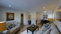 This 2-bedroom, 1-bathroom residence is thoughtfully laid out across a single floor, offering an efficient and comfortable living environment. The open-concept living and dining area serves as the heart of the home, featuring warm hardwood-style flooring that runs throughout and creates a cohesive, welcoming atmosphere. Recessed lighting and flush-mount fixtures provide consistent illumination, complementing the neutral wall tones that lend the space a clean, modern aesthetic.

The living area is generously proportioned, with ample room for seating arrangements centered around a coffee table, making it ideal for both relaxing and entertaining. A decorative corner accent adds a touch of personality to the space. Adjacent to the living area, the dining space accommodates a full dining set and flows naturally into the rest of the home.

A hallway leads to the two bedrooms, offering privacy from the main living areas. Overhead HVAC vents are visible throughout, ensuring year-round climate comfort. White baseboards and trim provide a crisp contrast against the flooring and walls, adding a polished finish to every room.

Overall, the layout maximizes functionality within its footprint, making this a practical and stylish home suited for a range of lifestyles.