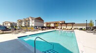Located at 950 Brushfield Dr in Galloway, Ohio, this single-floor residential unit is part of a well-appointed multi-building community. The property's standout amenity is a generously sized outdoor swimming pool with crystal-clear blue water, surrounded by a broad sundeck outfitted with lounge chairs for relaxing in the sun. A charming pergola anchors one end of the pool area, providing a shaded retreat, while the entire space is enclosed by a secure perimeter fence. The surrounding buildings feature traditional architectural styling with pitched rooflines, neutral exterior tones, and covered balconies that overlook the community grounds. The interior of the unit includes rooms with windows fitted with horizontal blinds, allowing for adjustable natural light. The single-story layout offers a straightforward and accessible floor plan. The community setting combines comfort and outdoor recreation, making the shared amenity spaces a central feature of the living experience. Situated in Galloway, the property benefits from a suburban atmosphere with easy access to local conveniences.