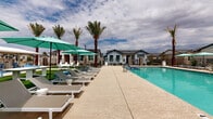 Located at 44900 W Bowlin Rd in Maricopa, Arizona, this single-level outdoor amenity space offers a well-appointed community retreat designed for relaxation and recreation in the Sonoran Desert setting. At the heart of the space is a generously sized resort-style swimming pool with crystal-clear turquoise water, accessible via entry steps and equipped with an ADA-compliant pool lift to ensure accessibility for all residents. Surrounding the pool is a spacious concrete sun deck furnished with modern white-framed lounge chairs and teal shade umbrellas, providing ample space for sunbathing and outdoor leisure. Adjacent to the pool deck, a vibrant green lawn area offers a versatile open-air gathering space, dotted with clusters of tall mature palm trees that lend a tropical ambiance to the desert surroundings. White Adirondack chairs and accent tables are thoughtfully arranged throughout the lawn, creating comfortable seating vignettes. An additional patio area features outdoor dining furniture, ideal for casual gatherings. The perimeter is enclosed by black iron fencing, providing both security and an open sightline to the surrounding residential neighborhood. The overall design balances modern aesthetics with functional outdoor living, making it a central social hub for the community.