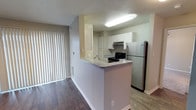 This two-floor residence offers a thoughtfully designed layout that balances functionality and comfort. The kitchen is a standout feature, showcasing a peninsula with light granite-style countertops that provide both workspace and a natural divider between the kitchen and the adjacent living area. White upper cabinetry offers ample storage, while the stainless steel refrigerator and black electric range provide a clean contrast that adds a modern touch. An under-cabinet range hood contributes to the kitchen's practical design.

The flooring transitions between two distinct materials — dark hardwood-style planks in the living area and lighter wood-look flooring in the kitchen — adding visual interest and clearly defining each zone. Neutral-toned walls in warm grey and beige tones create a cohesive and inviting atmosphere throughout the space.

A sliding glass door fitted with vertical blinds allows natural light to filter into the living area while providing access to an outdoor space. The two-floor layout offers additional living or sleeping space above, adding to the overall versatility of the residence. Clean lines, neutral finishes, and updated fixtures give the home a well-maintained, move-in-ready appeal.