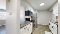 This single-floor, 2-bedroom, 1-bathroom residence offers a thoughtfully designed layout that maximizes every square foot of its compact footprint. The interior is finished with consistent wood-look luxury vinyl plank flooring throughout, lending a cohesive and contemporary feel across all rooms.

The kitchen is a functional highlight of the home, featuring white shaker-style cabinetry with matte black hardware, granite-look countertops with a tile backsplash, and a full suite of stainless steel appliances including a range, over-the-range microwave, and refrigerator. The kitchen connects openly to the living area, creating an efficient and social flow.

The living room is bright and welcoming, with two windows fitted with horizontal blinds that invite natural light and views of the surrounding neighborhood. A ceiling fan adds comfort and practicality to the space.

The primary bedroom offers a comfortable footprint with a window for natural light, while the second bedroom also features a window and a sliding closet with built-in rod storage. Both bedrooms are finished with neutral gray walls and wood-look flooring. A connecting hallway with white panel doors provides access to each room.

The bathroom is clean and modern, featuring a tub/shower combination with white tile surround, wood-look flooring, and matte black towel bar accents that tie into the home's overall design aesthetic.