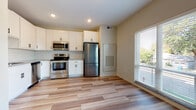 This single-floor unit offers a well-organized layout that balances functionality and modern design. The kitchen serves as a central highlight, outfitted with white shaker-style cabinetry, a classic white subway tile backsplash, granite-look countertops, and a full suite of stainless steel appliances, including a refrigerator, electric range, built-in microwave, and dishwasher. Light wood-style plank flooring extends throughout the main living areas, contributing to a clean, contemporary aesthetic.

The open layout connects the kitchen to the living area, which benefits from natural light through a large window fitted with horizontal blinds. A separate bedroom features soft carpeting, a dedicated closet with built-in wire shelving, and additional space for furnishings. The full bathroom is finished with wood-look tile flooring, a white shaker-style vanity with matte black hardware, a combined tub and shower unit, and a matte black towel bar for a cohesive, modern touch.

Additional features include an in-unit laundry area and a ceiling fan in the main living space. The unit's neutral color palette and consistent finishes create a bright, move-in-ready environment.