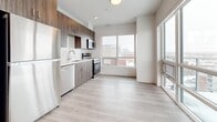 This well-designed 2-bedroom, 2-bathroom unit offers a functional and modern layout spread across a single floor. Light hardwood-style flooring runs consistently throughout, unifying the space and contributing to an airy, cohesive aesthetic.

The open kitchen is a standout feature, outfitted with wood-grain cabinetry extending to the ceiling, white quartz countertops, a geometric hexagonal tile backsplash, and a full suite of stainless steel appliances including a refrigerator, electric range, microwave, and dishwasher. The kitchen flows into the dining and living area, which is bathed in natural light from large windows and a sliding glass door that opens onto a private balcony with panoramic city views.

Both bedrooms are well-proportioned with clean white walls and windows that bring in ample natural light. The primary bedroom benefits from views of the surrounding urban landscape. A hallway with closet access connects the rooms efficiently.

Each bathroom features large-format tile flooring, a glass-enclosed walk-in shower with neutral stone-toned tile surround, a wood-tone vanity with a white countertop, and a mirror. The overall design is clean and contemporary, with a neutral palette that maximizes brightness throughout the unit.