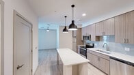 Located at 651 E 6th St in Tempe, Arizona, this thoughtfully designed 2-bedroom, 2-bathroom residence offers a clean, contemporary aesthetic throughout its single-floor layout. The open-concept kitchen serves as the heart of the home, showcasing flat-panel wood-tone cabinetry, a light blue subway tile backsplash, white quartz countertops, and a full suite of stainless steel appliances including a range, microwave, and dishwasher. A freestanding kitchen island with pendant lighting above provides additional prep space and a casual dining option, while light wood-look flooring flows seamlessly through the main living areas. The bedrooms are carpeted for comfort and each feature ceiling fans and dedicated closets. The primary bedroom includes a spacious walk-in closet with multi-level shelving and hanging rods for ample storage. The en-suite primary bathroom is finished with a floating wood vanity, quartz countertop, and a glass-enclosed walk-in shower with large-format tile. The second bathroom offers a tiled tub-shower combination with a matching wood vanity. Recessed lighting and clean white walls throughout maintain a bright, modern ambiance well-suited to the sunny Tempe environment.