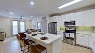 This single-floor residence is thoughtfully designed with a contemporary open-concept layout, seamlessly connecting the kitchen, dining, and living areas. The kitchen is a standout feature, equipped with stainless steel appliances including a French door refrigerator, electric range, built-in microwave, and dishwasher. Crisp white cabinetry pairs with a green geometric tile backsplash, while the expansive island with a double sink offers additional prep space and bar seating for multiple guests. Light wood-style flooring runs throughout the main living areas, enhancing the bright, airy atmosphere.

The living room benefits from natural light through large windows and a sliding glass door that opens to an outdoor area, complemented by a ceiling fan overhead. Two bedrooms provide comfortable retreats, each featuring ceiling fans, windows with exterior views, and plush carpeting. Both bathrooms are well-appointed with white vanities, wide mirrors, wood-style flooring, and direct access to spacious walk-in closets. The primary bathroom also includes a glass-enclosed shower. Recessed lighting throughout ensures consistent illumination, contributing to the clean, modern ambiance of the space.